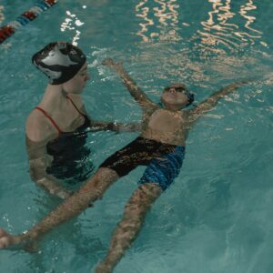 A child learning to swim with the guidance of an instructor in an indoor swimming pool.