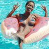 Young woman smiles and poses with peace signs while floating in a pool on a donut-shaped inflatable.