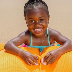 Happy young girl smiling on the beach, playing with an orange inflatable toy. Perfect summer fun.